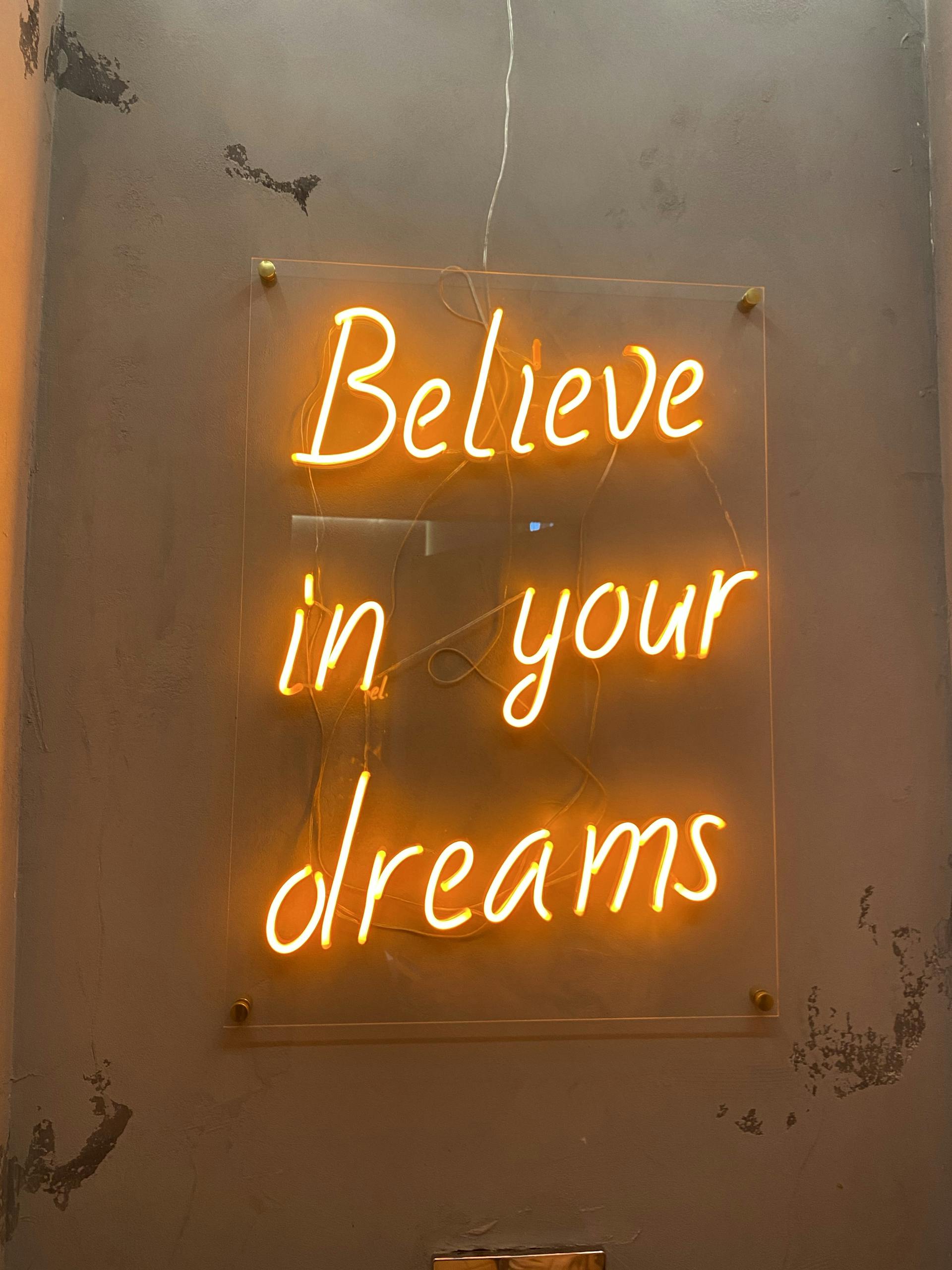 Bright neon sign on wall reading 'Believe in your dreams' in glowing yellow-orange.